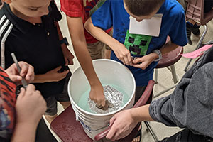 Students floating pennies in a tinfoil hat in a bucket