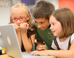 three elementary students huddled around a laptop