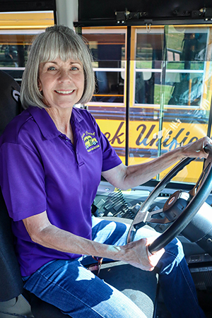 Woman school bus driver in purple shirt behind the wheel