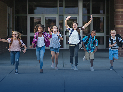 students running with backpacks in front of a school