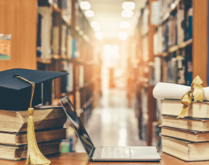 books, grad cap, and laptop sitting on a table in the library