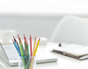 Colored pencils, laptop, and notebook sitting on a desk