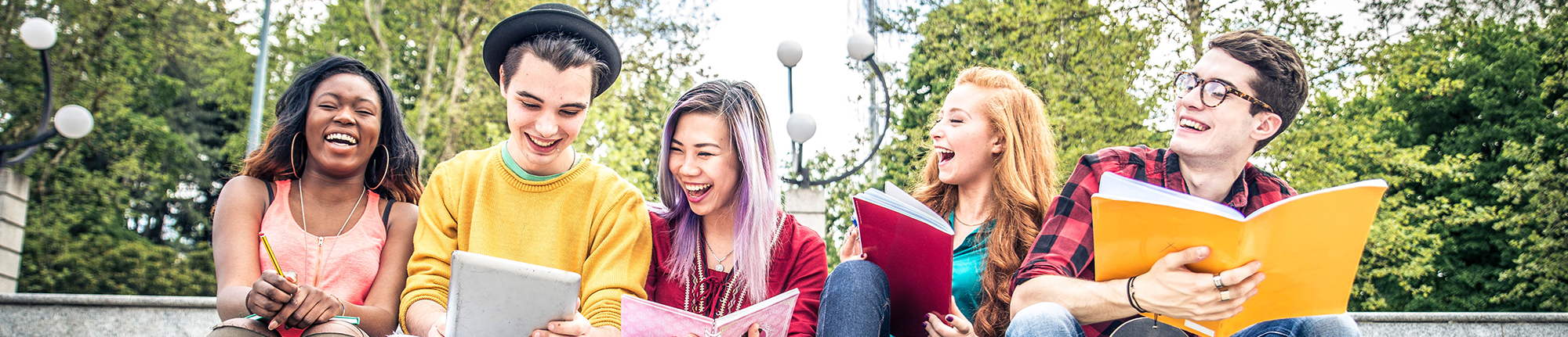 five students sitting on steps with notebooks laughing