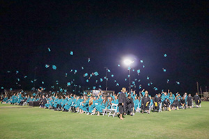 Outside nighttime photo of graduates throwing caps into the air