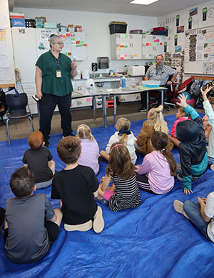 Students sitting on a tarp in the classroom and listening to the teacher