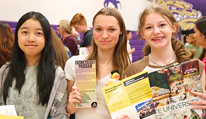 Three happy students holding college fair brochures