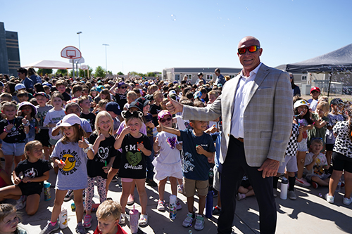 School representative giving a thumbs up next to group of students outside