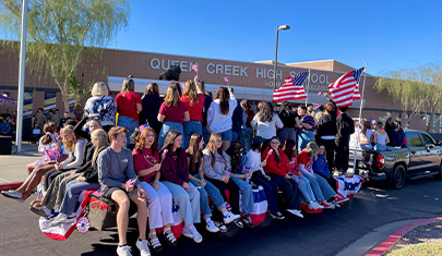 Students on a flatbed parade float being pulled in front of the High School