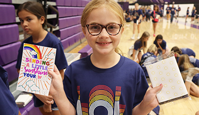 Happy school girl in glasses holding up notebooks