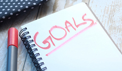 A pen next to a notebook that says the word Goals