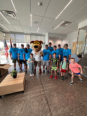 Group of men in blue tee shirts with dog mascot and four young children