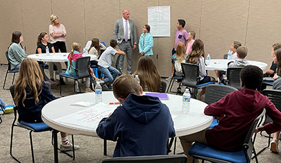 Students seated around tables watching three students and two adults