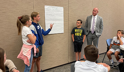 Three students and an adult talking in front of other students