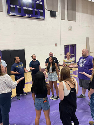 Students and teachers holding their hands out while forming a circle around a female student