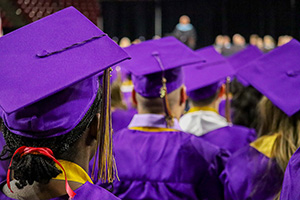 The backs of graduates wearing purple caps and gowns