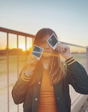 Girl at sunset, holding polaroid pictures to her face