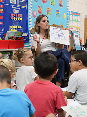 four elementary students in white shirts holding school supplies
